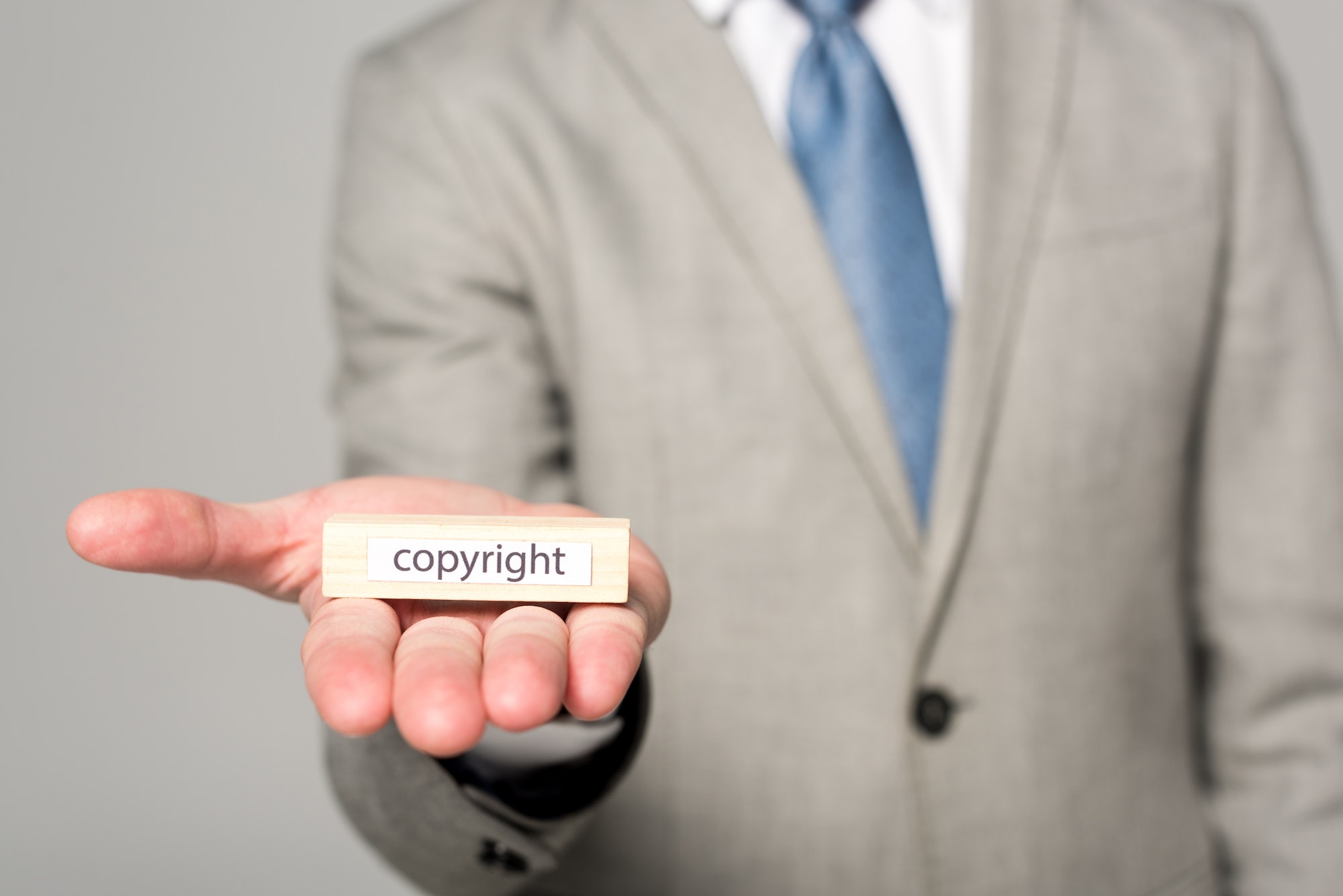 cropped view of businessman showing wooden block with word copyright isolated on grey