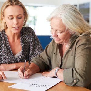 Female Friend Helping Senior Woman To Complete Last Will And Testament At Home